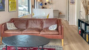 Ein braunes Ledersofa mit gemusterten Kissen, ein runder schwarzer Tisch und ein flauschiger Teppich in Rot und Grau.