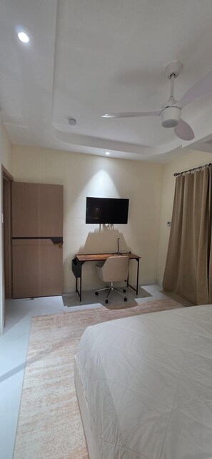 Una camera da letto con un letto, una scrivania con una sedia, una televisione e un ventilatore a soffitto.