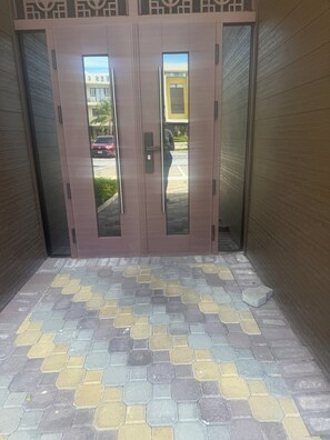 A set of double doors with a reflective glass panel, leading to a paved entrance area with a patterned tile floor. - Coastal Retreat. Beach life. Luxury 1 BR apartment at the Paradisiac Beach Club. (Richmond Estate)