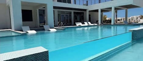A swimming pool with lounge chairs, a covered area with a railing, and a building with large windows.