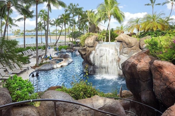 A resort pool with a waterfall, palm trees, and a beach view. - Charming 1-bedroom condo with AC in beautiful Honolulu (Honolulu)