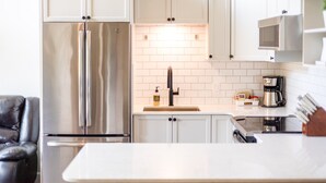 Une cuisine moderne avec des meubles blancs, un réfrigérateur en acier inoxydable, une machine à café et un bloc à couteaux.
