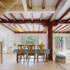 Ein Essbereich mit Holztisch und -stühlen, großen Fenstern und einer Decke mit sichtbaren Holzbalken.