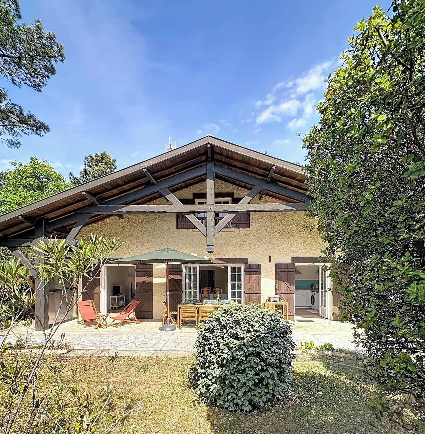 Ein zweistöckiges Gebäude mit geneigtem Dach, Holzbalken und einer Terrassenanlage mit Gartenmöbeln.