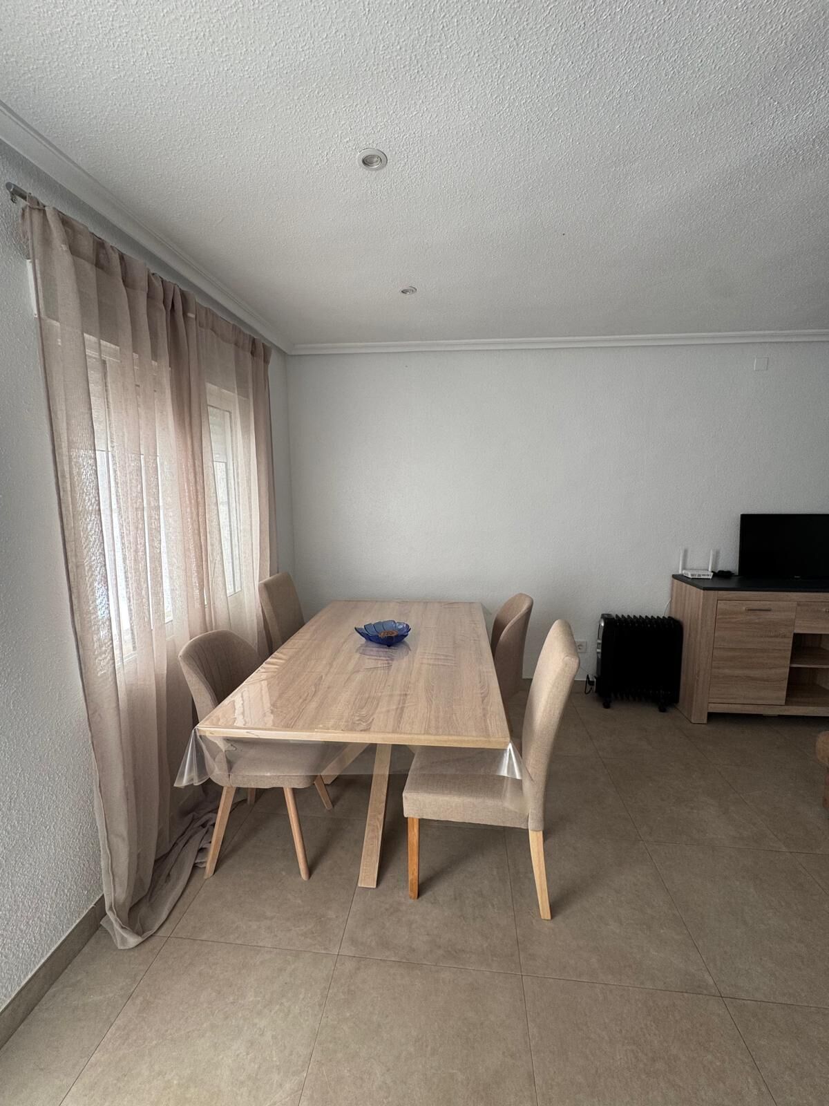 Un comedor con una mesa y sillas de madera, un cuenco azul, un radiador y un mueble para televisor.