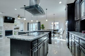 A modern kitchen with a large island, dark cabinetry, and pendant lighting.