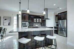 A modern kitchen with dark wood cabinets, stainless steel appliances, and a granite island with bar stools.
