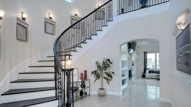 Ein modernes Interieur mit einer schwarz-weißen Treppe, einer großen Topfpflanze und einem geräumigen Wohnbereich inklusive Sofa und Fernseher.