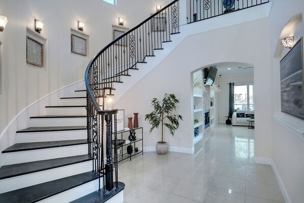 A modern interior with a black and white staircase, a large potted plant, and a spacious living area with a sofa and TV.