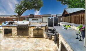 An outdoor kitchen area with a stone countertop, a grill, and a built-in oven.