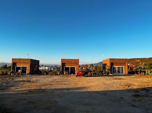 Een rij bakstenen gebouwen met open garage deuren, een rode auto ervoor geparkeerd, en een strakblauwe lucht.
