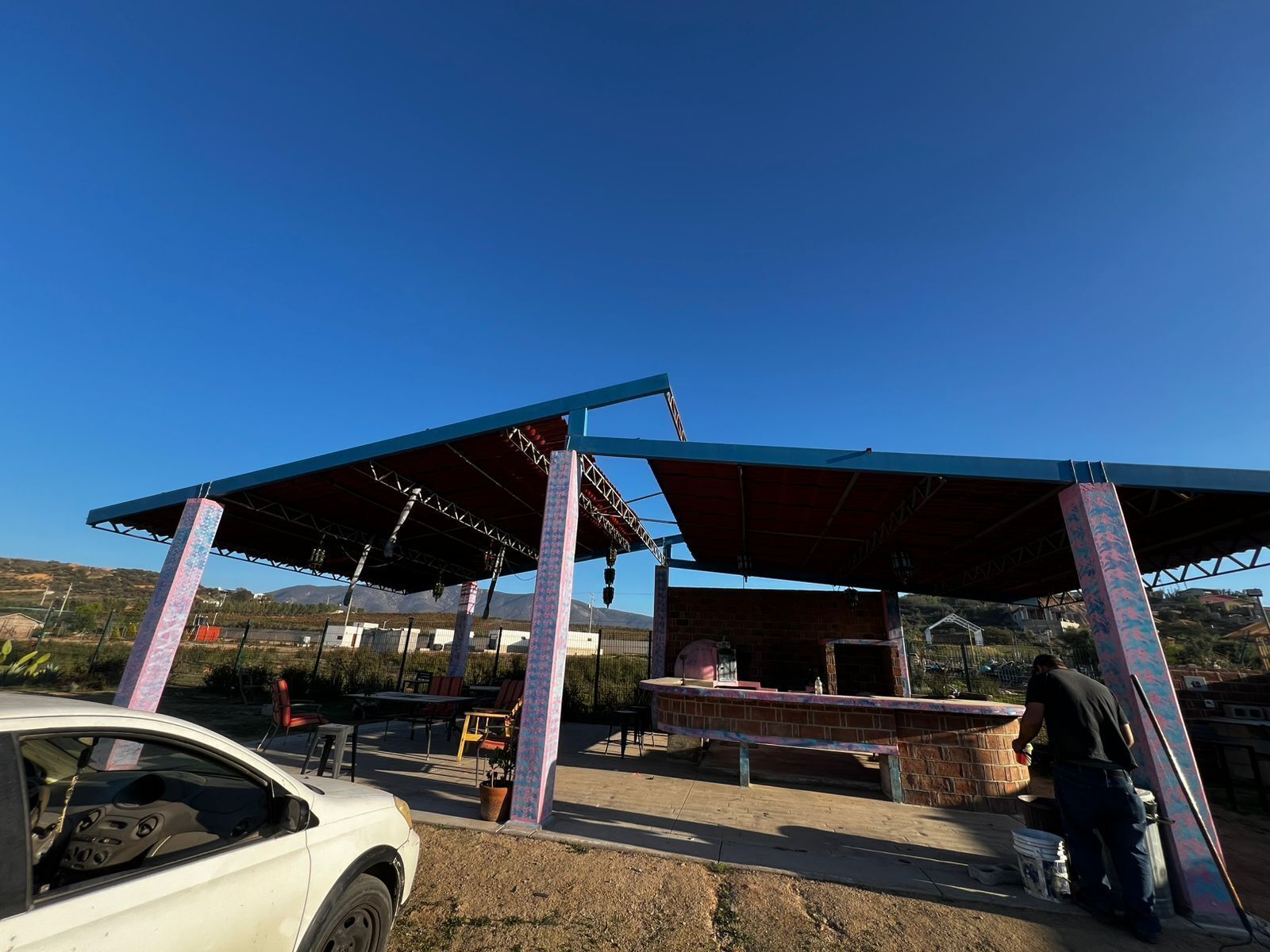A covered outdoor area with a brick structure, possibly a barbecue or grill, and a car parked nearby.