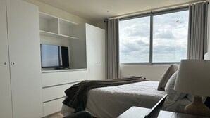 Hotellihuone, jossa on sänky, työpöytä kannettavalla tietokoneella, hyllyllä oleva televisio ja ikkuna, jossa on verhot.