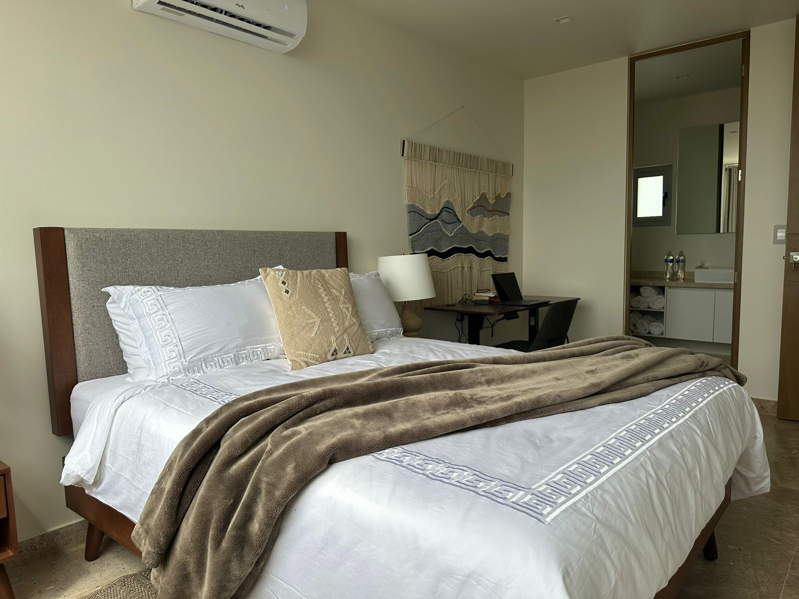 A hotel room with a bed, a desk, a chair, a lamp, and a bathroom visible through an open door.