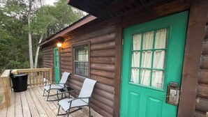 Eine Holzhütte mit grüner Tür, einer Veranda mit Schaukelstühlen und einem Mülleimer.