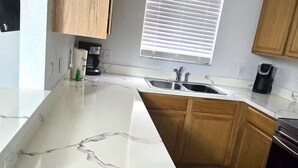 A kitchen with wooden cabinets, a white marble countertop, a sink, and a window with blinds. - 324 Palermo Villa 30 min to Disney and Universal (Davenport)