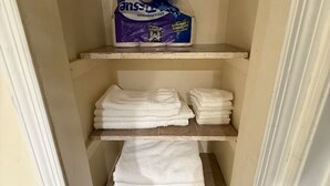 A small storage closet with shelves, a toilet paper package, and folded towels.