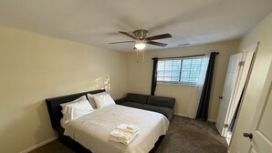 A bedroom with a bed, a ceiling fan, a window with blinds, and a door.