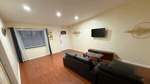 A living room with a sofa set, a flat-screen TV mounted on the wall, and a door with a window.