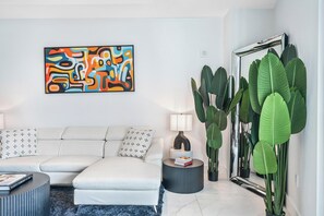 Ein modernes Wohnzimmer mit einer Couch, einem Couchtisch, einer Lampe, einem großen Spiegel und einem farbenfrohen, abstrakten Gemälde.
