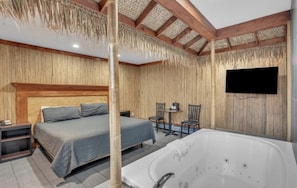 Une chambre comprenant un lit, un coin salon avec des fauteuils et une table, une grande baignoire blanche et un téléviseur fixé au mur.