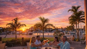 A group of people toasting at a table with a view of a marina and sunset.