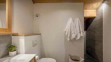 A bathroom with a toilet, a sink, a potted plant, a towel rack, and a trash bin.