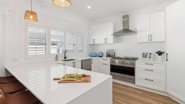 A modern kitchen with white cabinetry, a central island, a stove, and a sink.