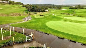 A golf course with a water hazard, a bridge, and surrounding greenery.
