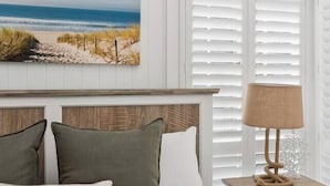 A bedroom with a bed, pillows, a nightstand, a lamp, and a beach-themed painting on the wall.