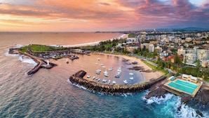 An aerial view of a coastal city with a marina, buildings, and a beach.