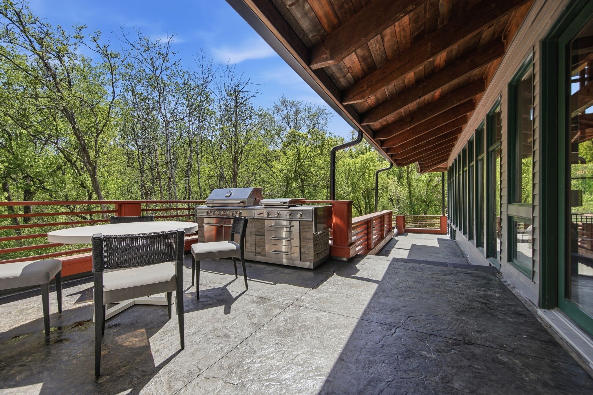 An outdoor patio with a grill, seating, and a view of the forest.