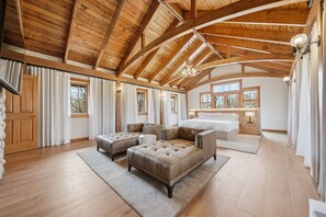 Une chambre spacieuse avec un grand lit, deux canapés capitonnés, un plancher en bois et un plafond en bois particulièrement haut.
