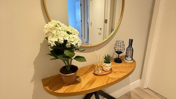 Une console en bois, ornée d’un miroir rond, d’une plante en pot et d’objets décoratifs.