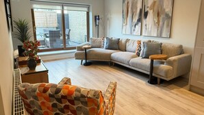 Un salon moderne avec un canapé d’angle, un fauteuil à motifs et des œuvres d’art abstraites accrochées au mur.