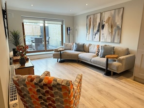 Ein modernes Wohnzimmer mit einem Ecksofa, einem gemusterten Sessel und abstrakter Wandkunst.
