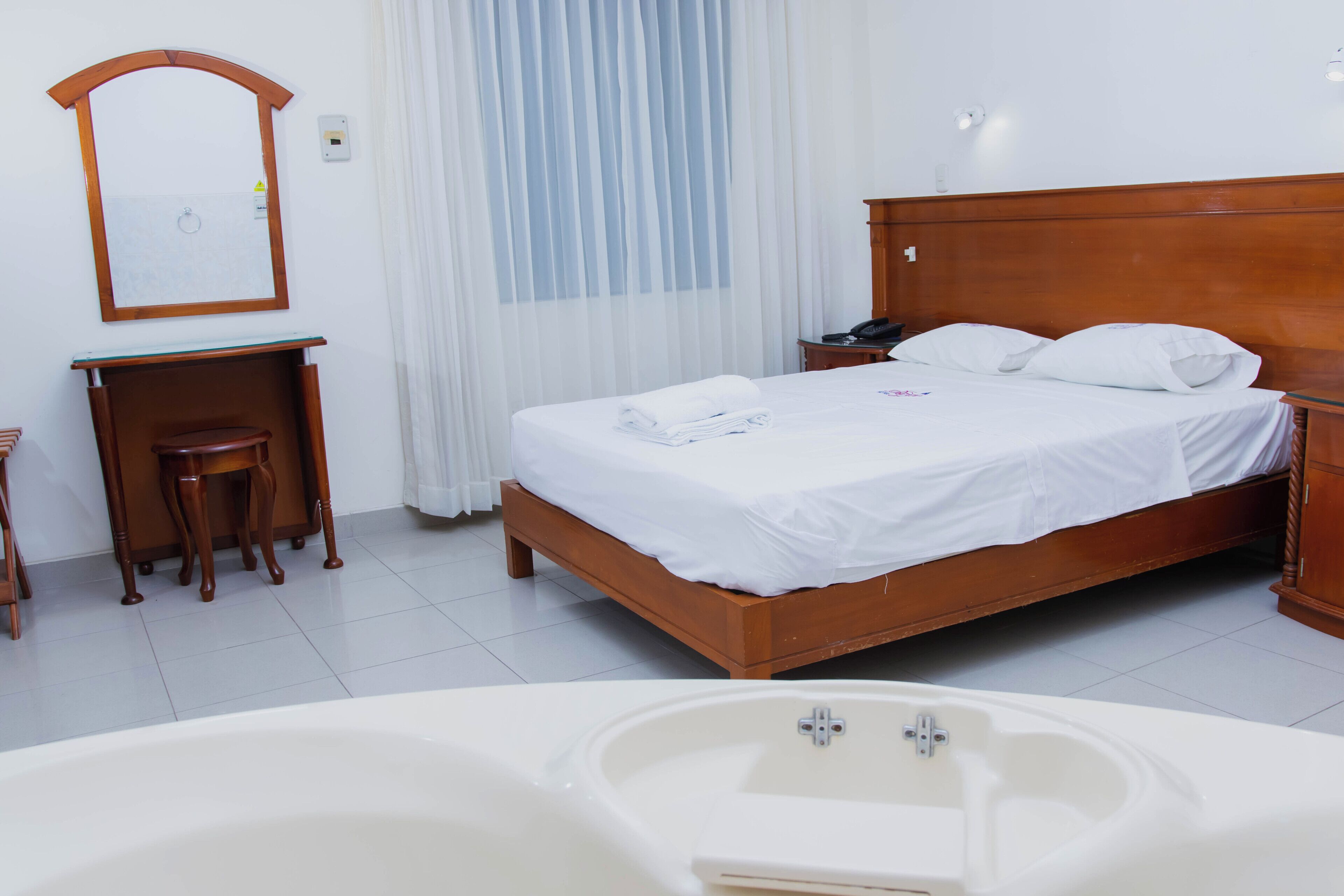 Habitación de hotel con cama y escritorio de madera, espejo, teléfono y bañera.