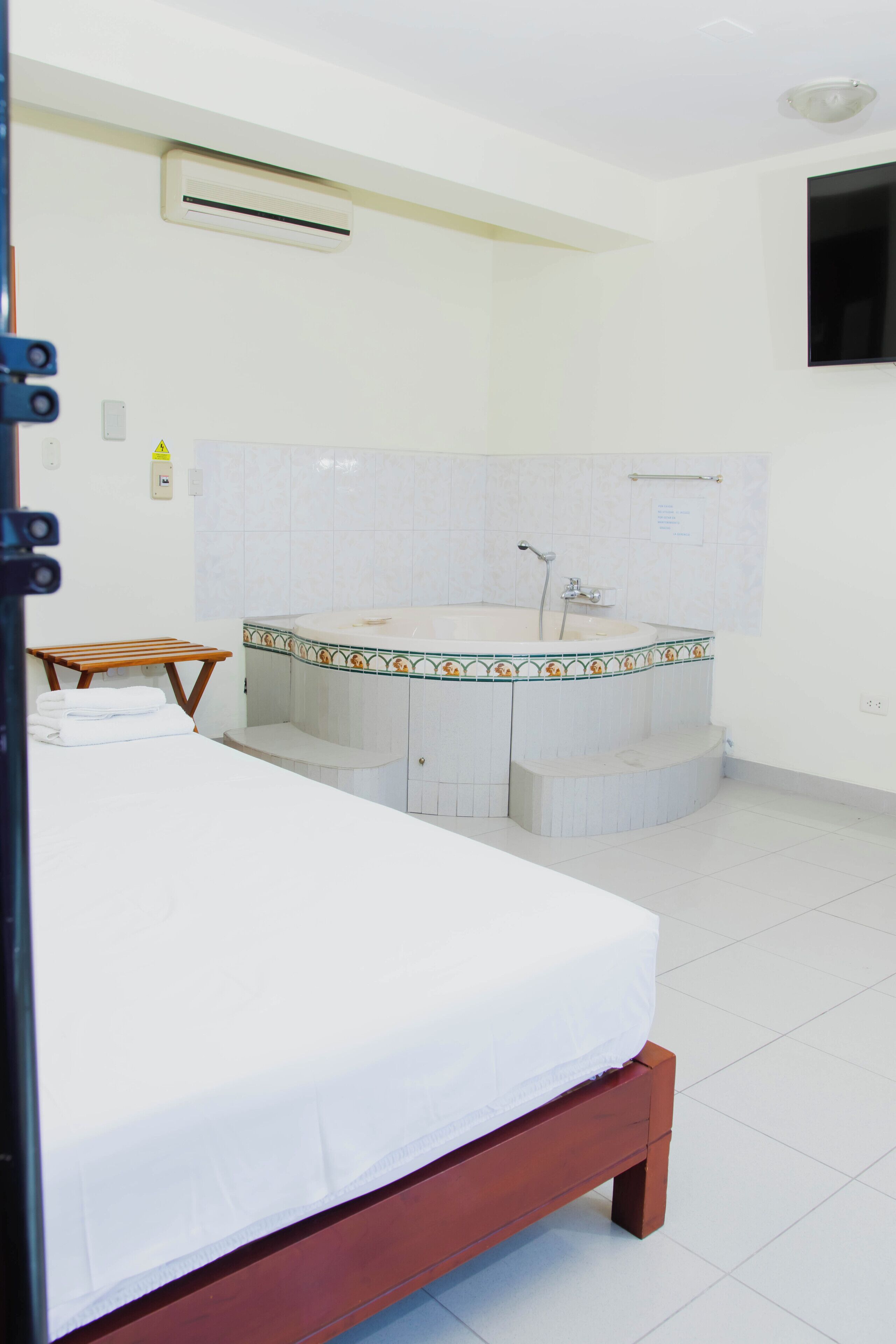 Habitación de hotel con una cama, baño con bañera y televisor montado en la pared.