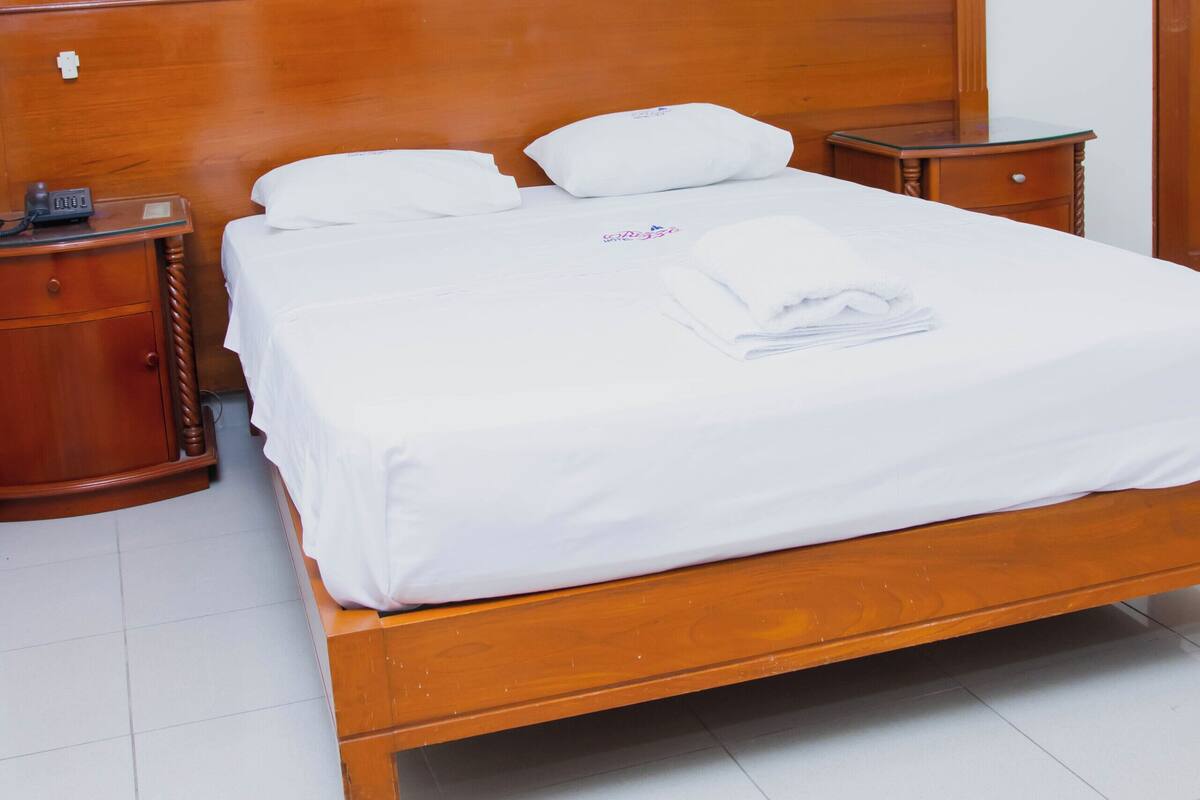 A neatly made bed with white linens, a wooden headboard, and two bedside tables with clocks.