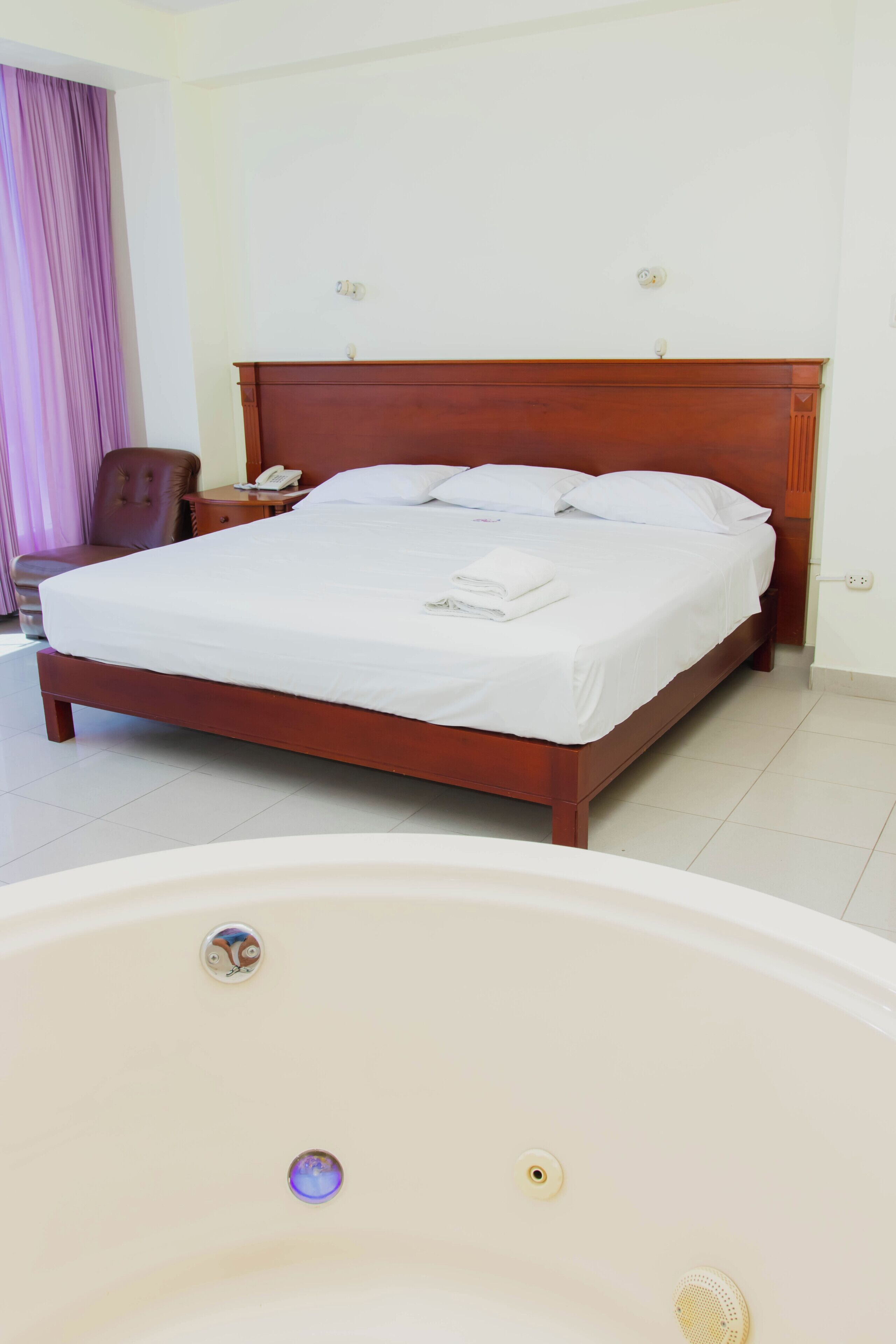 Una habitació d'hotel amb un llit de fusta, un telèfon a la nit, una cadira i una banyera.