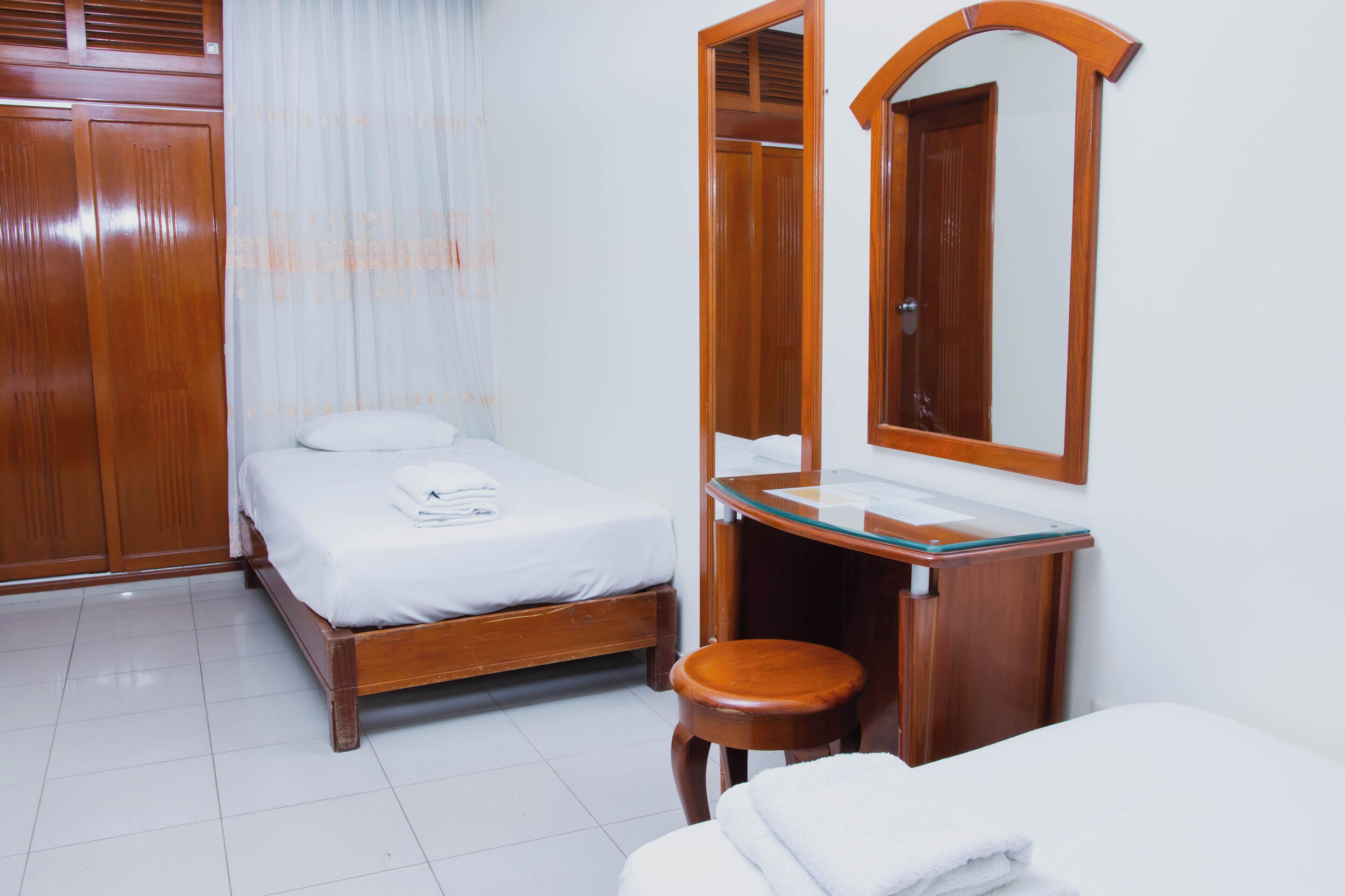 Una habitación de hotel con cama, armario de madera, baño con espejo y un taburete pequeño.