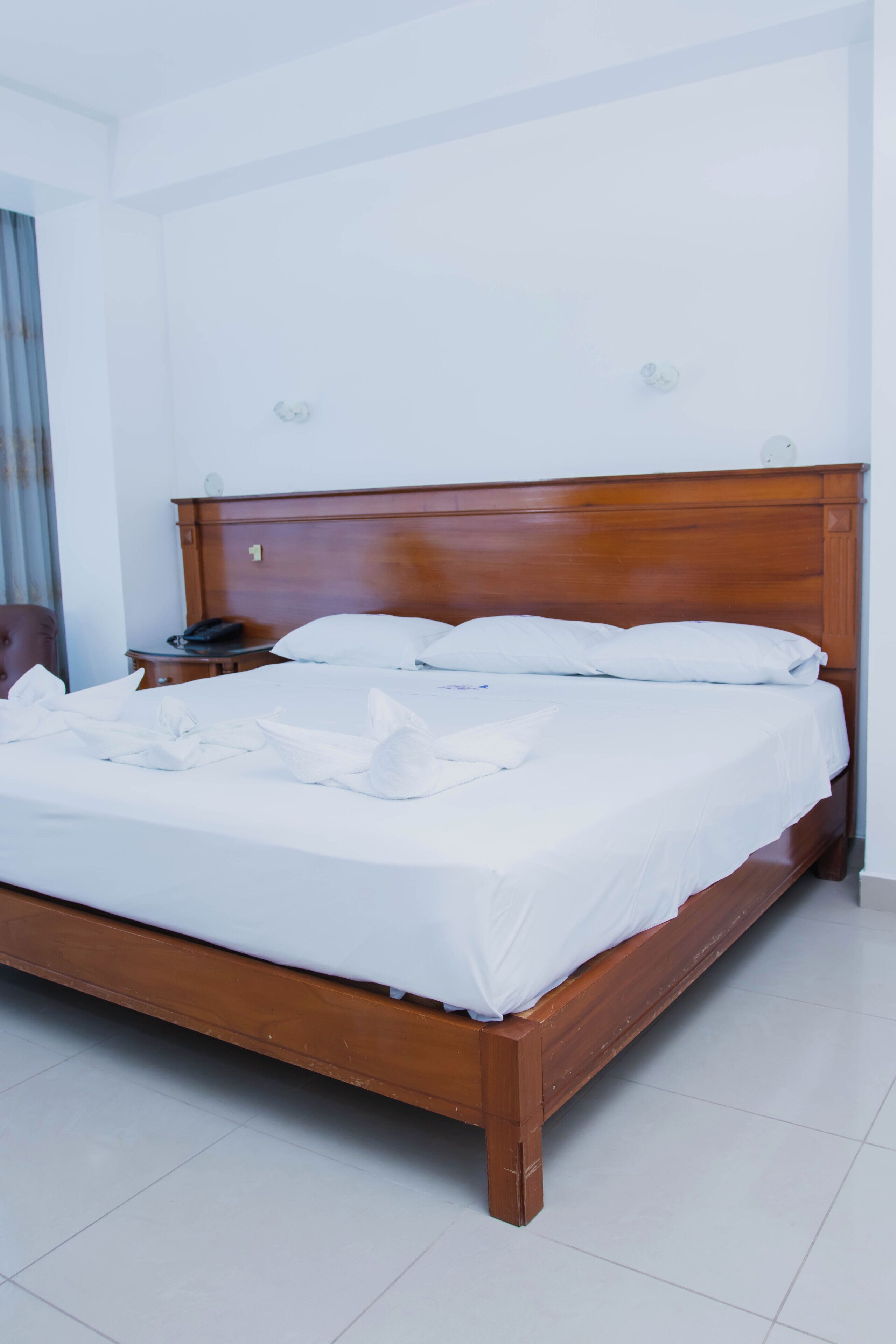 A neatly made bed in a hotel room with a wooden headboard, a bedside table with a lamp, and a chair.
