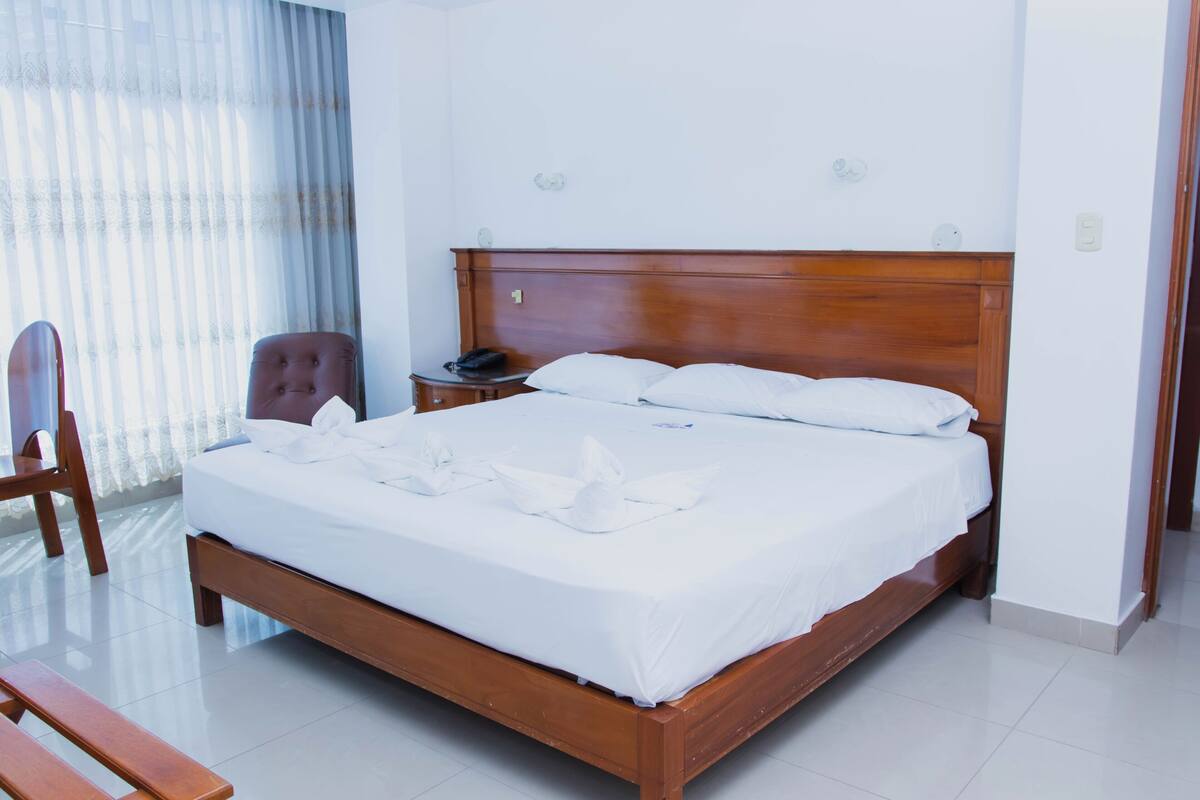 A neatly made bed with a wooden headboard, a bedside table with a phone, and a chair.