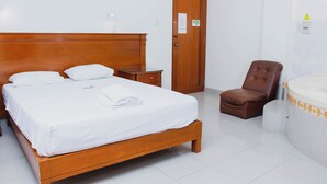 Una habitación de hotel con una cama de madera, un sillón de cuero marrón, una mesita de noche pequeña y un baño con bañera.
