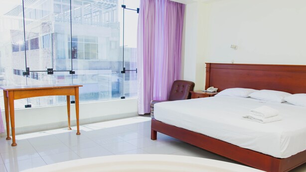 Habitación de hotel con una cama grande, una mesa de madera, una silla, una mesita de noche con teléfono y una ventana con vistas a edificios.