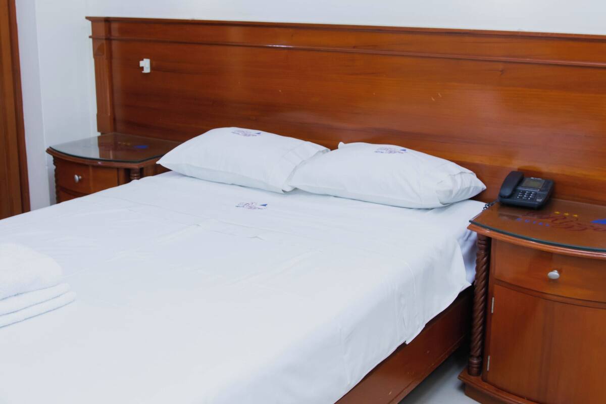 A neatly made bed with white linens, a wooden headboard, and a bedside table with a telephone.