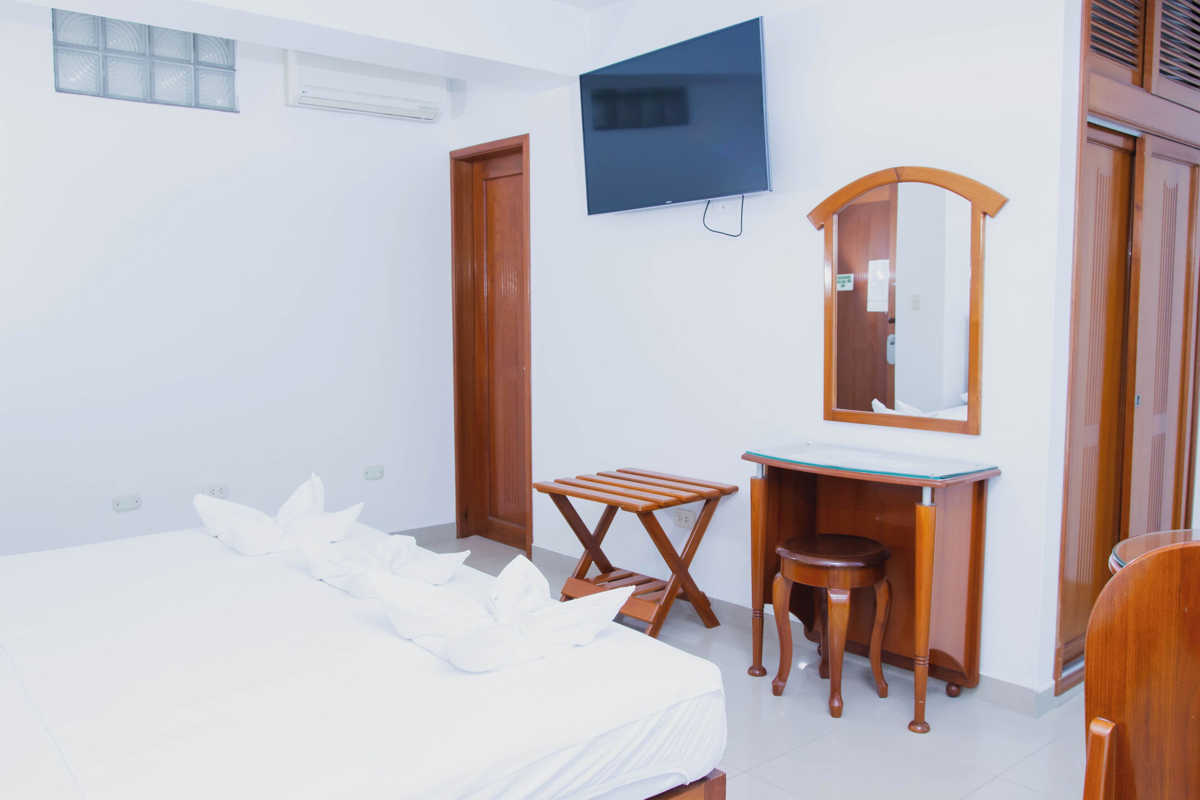 Un dormitorio con una cama, un escritorio de madera, un espejo y un televisor en la pared.