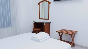 A hotel room with a bed, a wooden stool, a wooden side table, a mirror, and a television mounted on the wall.
