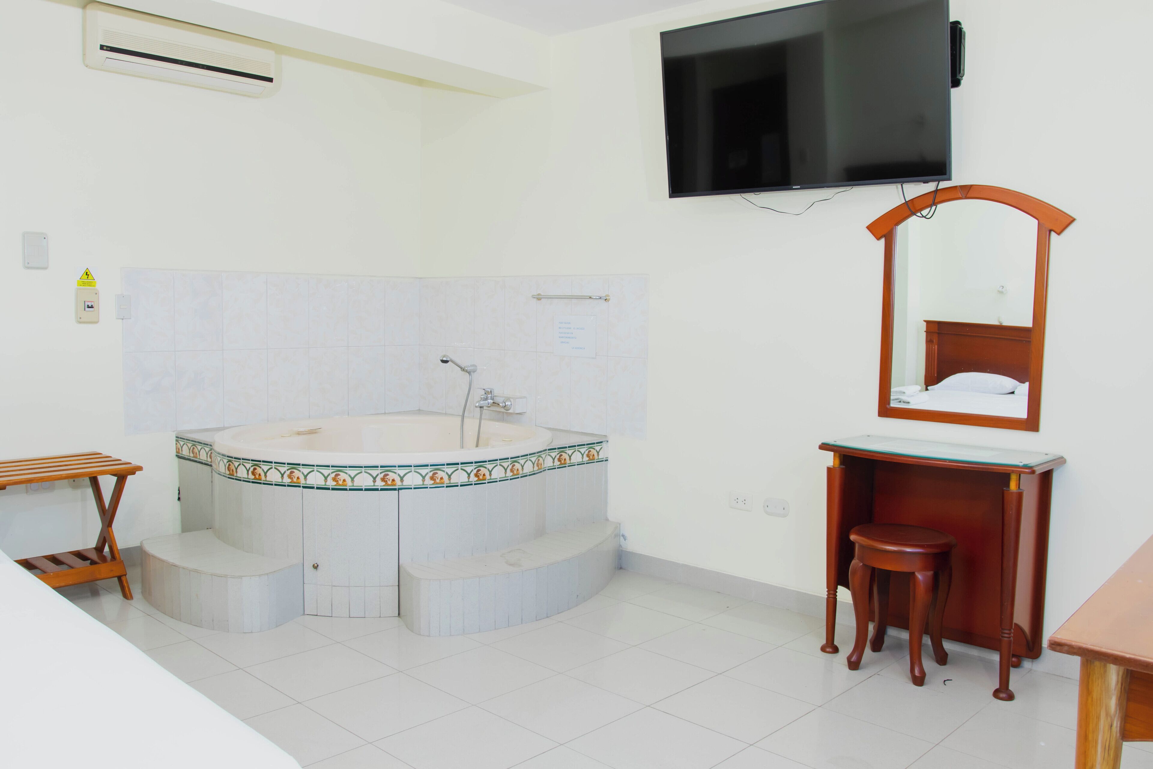 Une salle de bain dotée d’une grande baignoire, d’un meuble-lavabo en bois, d’un miroir et d’un téléviseur fixé au mur.