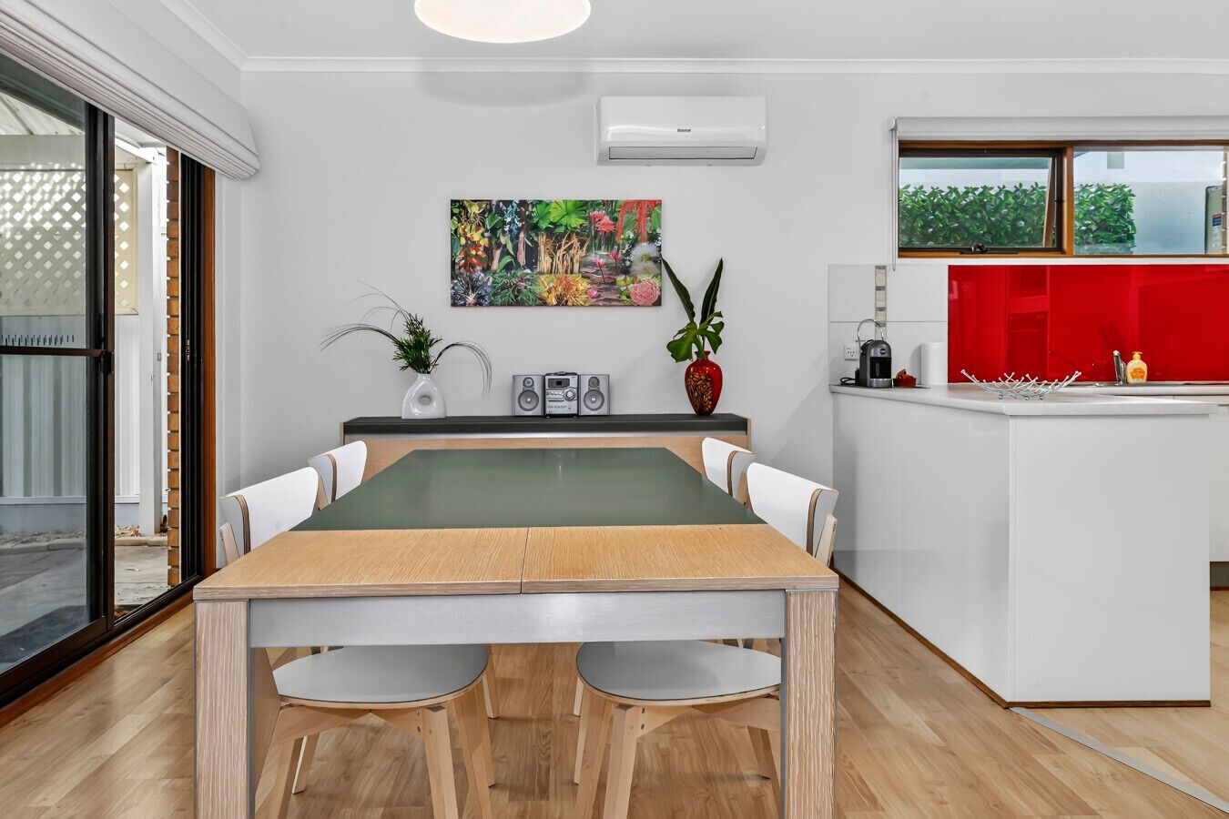 A modern kitchen with a dining area, featuring a large table, chairs, a kitchen island, and a colorful painting on the wall.